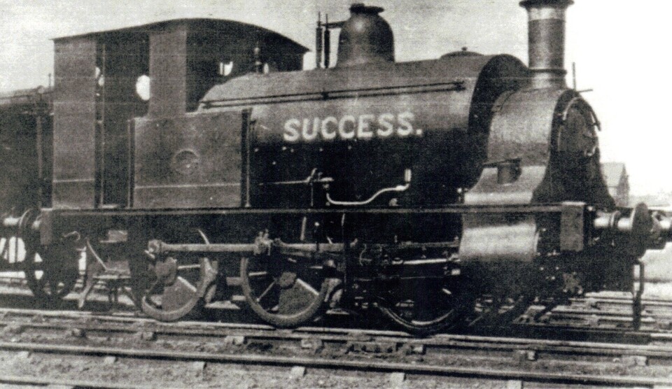 Black and white photo of an old steam locomotive on train tracks with the word "SUCCESS" painted in large letters on its side.